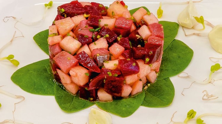 Ein Tartare aus roten und weißen Würfeln auf Spinatblättern, garniert mit Sprossen und Klecksen einer hellen Creme.