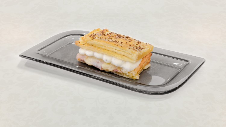 Blätterteigschnitte mit Sahne- und Schichtenfüllung auf einem länglichen schwarzen Teller, detailreiche Tischdecke im Hintergrund.