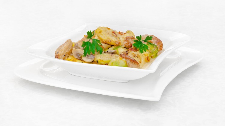 Überbackene Kartoffelscheiben mit Pilzen, Brokkoliröschen und Petersilie, angerichtet in einer weißen Auflaufform auf weißem Teller.
