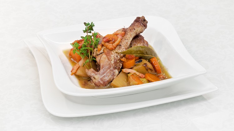 Hühnerkeule mit Karotten, Kartoffeln, Speckstreifen und Kräutern in heller Sauce auf weißem Teller angerichtet.