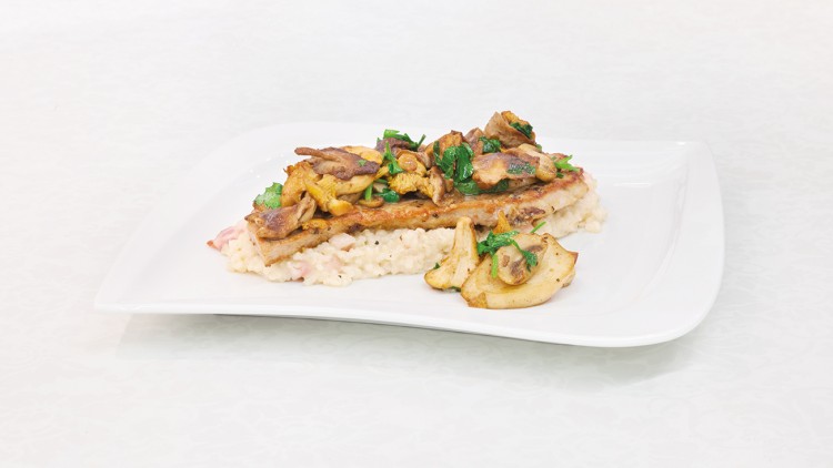 Gericht aus cremigem Risotto, gebratenem Fleisch und Pilzen, garniert mit frischen Kräutern auf weißem rechteckigem Teller.