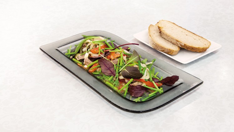 Ein rechteckiger Teller mit Salat aus grünem Gemüse, roten Blättern und Fleisch neben einem Teller mit zwei Brotscheiben.