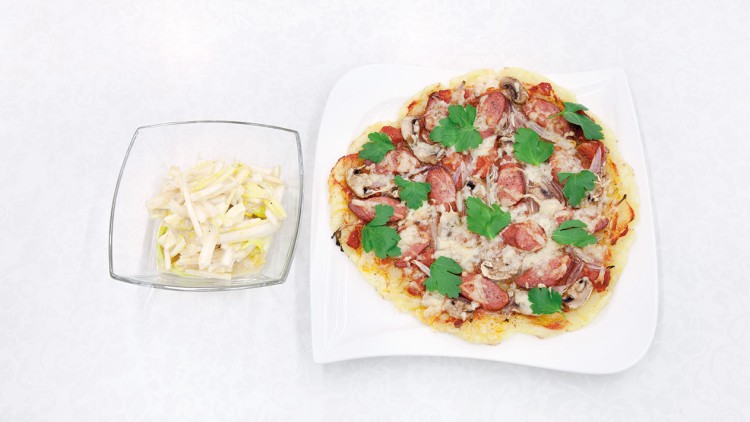 Runde Pizza mit Käse, Salami, Petersilie und Pilzen auf einem weißen Teller, daneben Chicoréesalat in einer Glasschale.