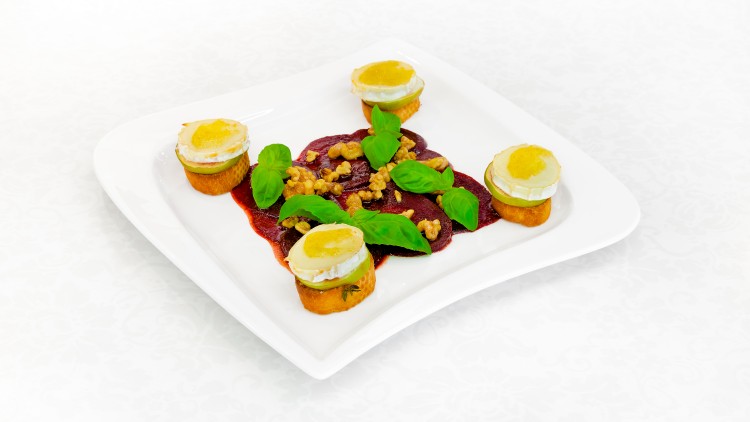Gebratene Süßkartoffelscheiben mit Ziegenkäse, Rote-Bete-Scheiben, Basilikumblättern und Walnüssen auf einem weißen Teller.