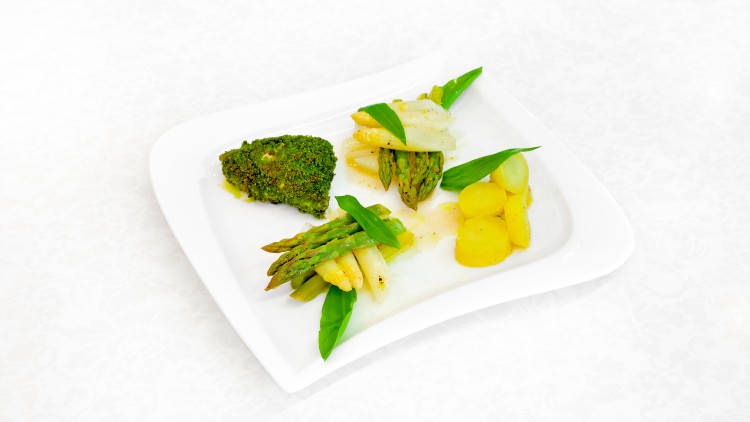 Auf einem weißen Teller liegen gratinierter Fisch, grüner und weißer Spargel, Kartoffelscheiben und Bärlauchblätter.