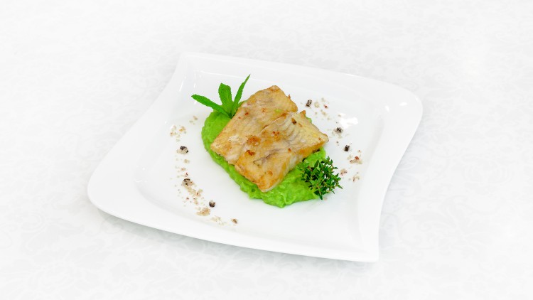 Ein eckiger Teller mit gebratenem Fischfilet auf grünem Püree, dekoriert mit Kräutern, Minzblatt und zerstoßenem Pfeffer.