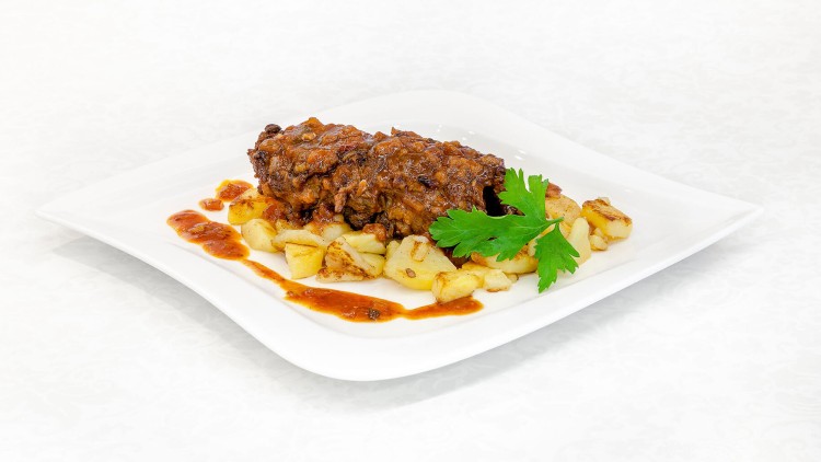 Ein rechteckiger Teller mit Rinderroulade, Bratkartoffeln, roter Soße und einem Petersilienzweig auf weißem Untergrund.