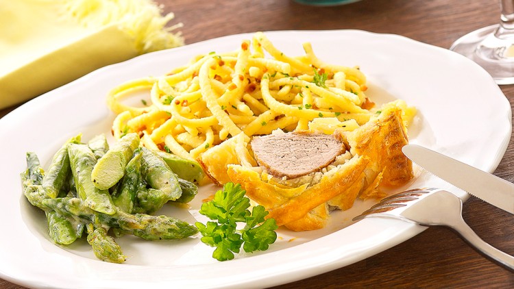Weißer Teller mit einem Filet im Blätterteig, grünen Bohnen, Spätzle, daneben eine gelbe Serviette, Salz, Pfeffer und Weißwein.