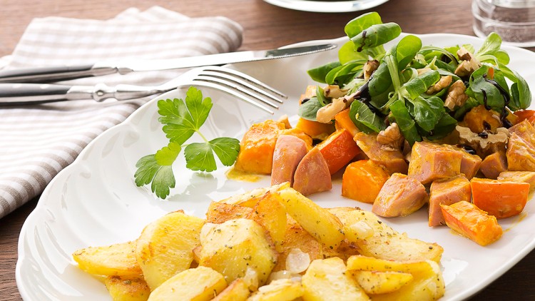 Auf einem weißen Teller liegen gebratene Kartoffelscheiben, Kürbisstücke, Feldsalat mit Walnüssen und eine Petersiliegarnitur.