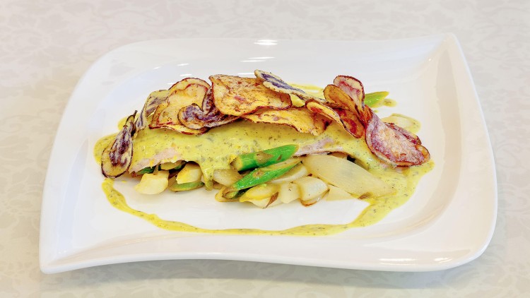 Gebratener Spargel und grüne Bohnen mit gelber Kräutersoße, garniert mit knusprigen Kartoffelchips auf weißem Teller.