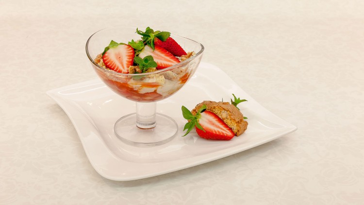 Dessert im Glas mit Erdbeeren, Sahne und Biskuitstücken, angerichtet auf weißem Teller mit zusätzlicher Erdbeere und Gebäck.