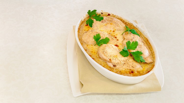 In einer weißen Auflaufform liegt überbackenes Hähnchen mit knuspriger Kruste, verziert mit frischen Petersilienblättern.