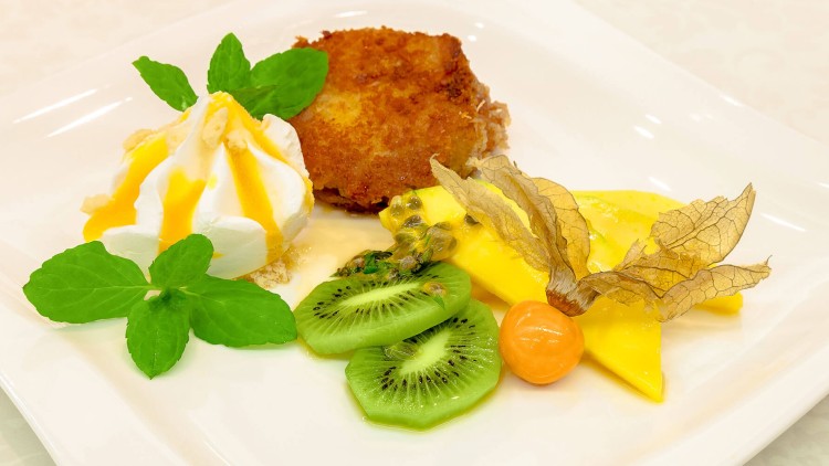 Dessertteller mit Kiwi, Mango, Physalis, frittiertem Gebäck, Sahnetupfer mit Soße und frischen Minzblättern.