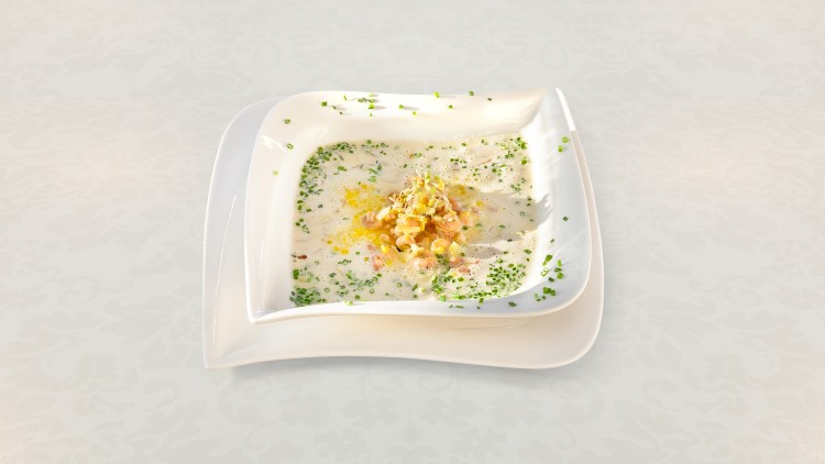 Cremige Suppe in weißem Teller mit Schnittlauchringen, goldenen Krümeln und Garnitur aus gehackten Nüssen auf hellem Untergrund.