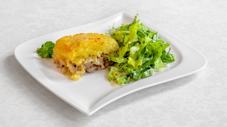 Ein Stück überbackener Auflauf mit Hackfleisch und Käse neben grünem Salat auf einem weißen Teller mit Petersilienzweig.