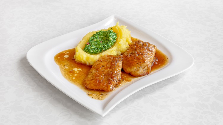Zwei Stücke gebratener Fisch in brauner Soße mit Kartoffelpüree und grünem Pesto auf einem weißen Teller.