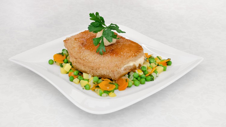 Panierter Käse mit flüssiger Füllung auf gedünstetem Gemüse aus Erbsen, Karotten und Kartoffelwürfeln mit Petersiliengarnitur.