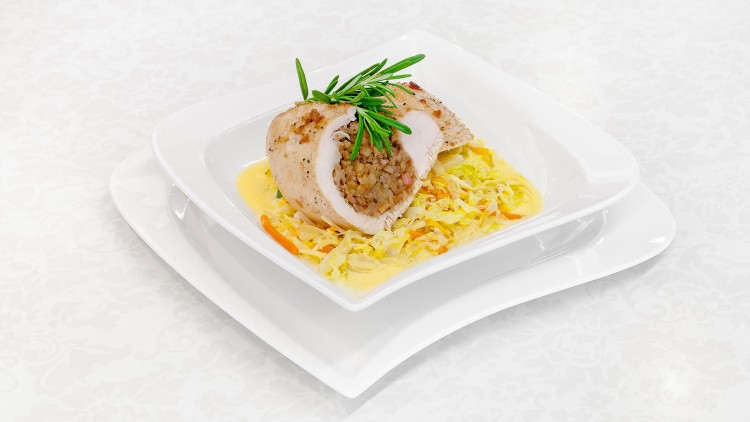 Gefüllte Hähnchenbrust mit Rosmarin auf Rahmwirsing und feinen Gemüsestreifen, angerichtet auf weißem Porzellangeschirr.