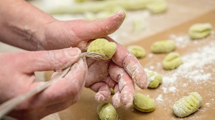 Hände formen grüne, mehlbestäubte Gnocchi und prägen mit einer Gabel Rillen in den Teig auf einer bemehlten Unterlage.