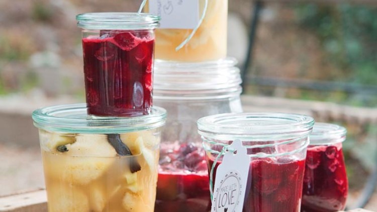 Mehrere Einmachgläser mit eingekochtem Obst wie Birnen und roten Beeren stehen auf einer Holzkiste im Freien.