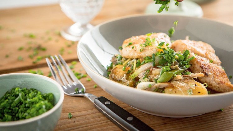 Gericht mit gebratenem Hähnchen, Kartoffeln, Gemüse und Schnittlauch in einer Schale, daneben ein Schälchen mit Schnittlauch.
