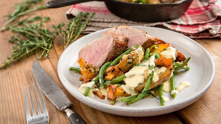 Auf einem Teller liegen aufgeschnittenes Fleisch, grüne Bohnen, Pfifferlinge, Kartoffelscheiben und helle Sauce, mit Kräutern dekoriert.