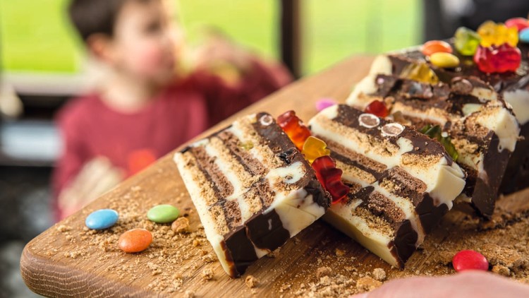 Schokoladentorte mit bunten Schokolinsen und Gummibärchen dekoriert liegt auf einem Holzbrett, im Hintergrund unscharfe Szene.