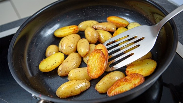 Bratkartoffeln in einer schwarzen Pfanne werden mit einem silbernen Pfannenwender angehoben.
