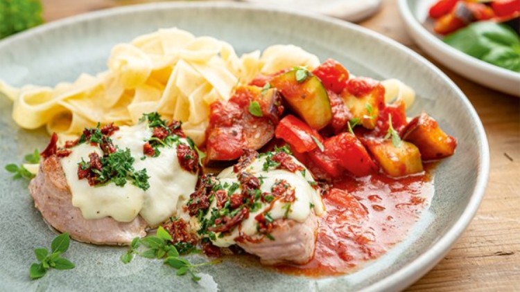 Ein grauer Teller mit Nudeln, überbackenem Fleisch mit Kräutern und Tomatensauce sowie gebratenem Gemüse.
