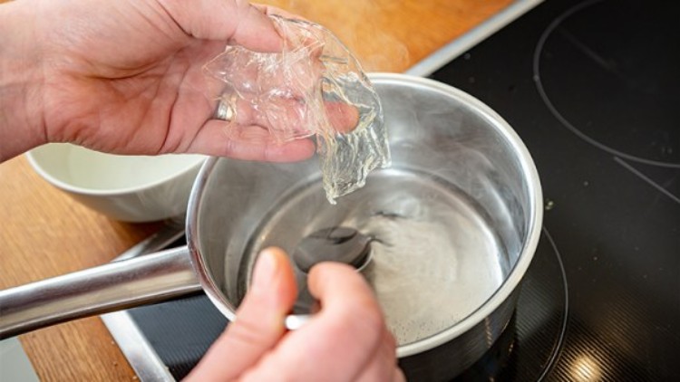 Ein Blatt Gelatine wird in einem kleinen Topf mit erhitztem Wasser auf einem Herd aufgelöst.