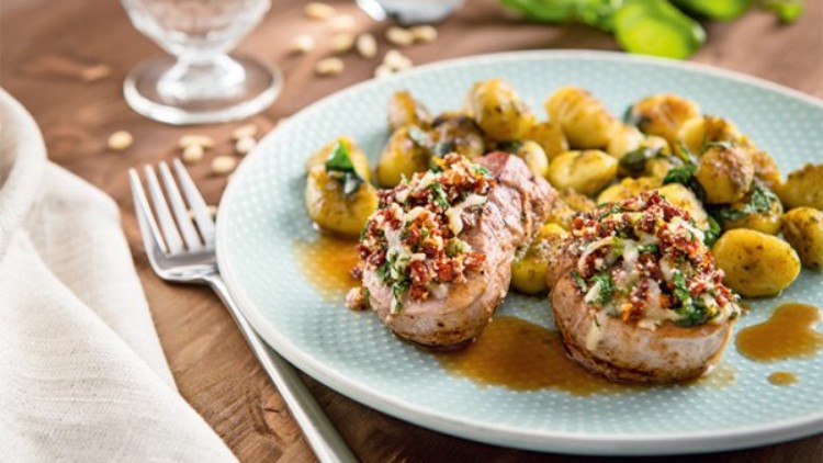 Angerichteter Teller mit zwei Medaillons, Tomatenkruste, brauner Sauce und goldbraunen Gnocchi, Tischdeko im Hintergrund.