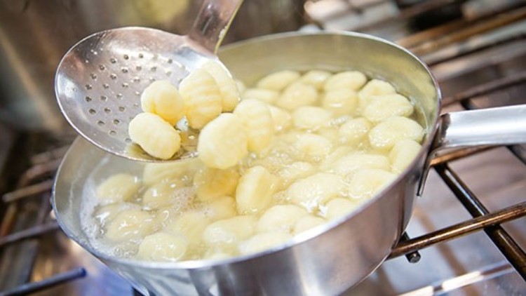 In einem Metalltopf auf einem Herd werden Gnocchi in heißem Wasser gekocht und mit einem Schaumlöffel herausgehoben.