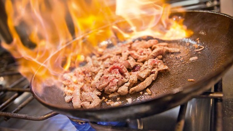 Geschnetzeltes Fleisch wird in einer schwarzen Pfanne auf einem Gasherd mit großer Flamme angebraten.