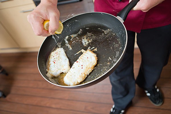 Zwei gebratene Fischfilets in einer Pfanne werden mit frischem Zitronensaft beträufelt.