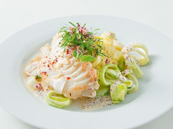 Gegrilltes Fischfilet mit Senfsoße, Lauchringen, Kartoffelpüree und frischem Dill auf einem weißen Teller angerichtet.