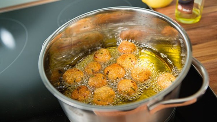 Runde Falafelbällchen werden in einem Topf mit heißem Öl auf einem Herd frittiert, daneben eine Zitrone und eine Ölflasche.