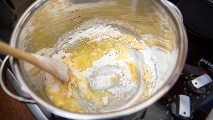 Ein Topf auf einem Herd, darin werden Butter und Mehl mit einem Holzlöffel zu einer Mehlschwitze verrührt.