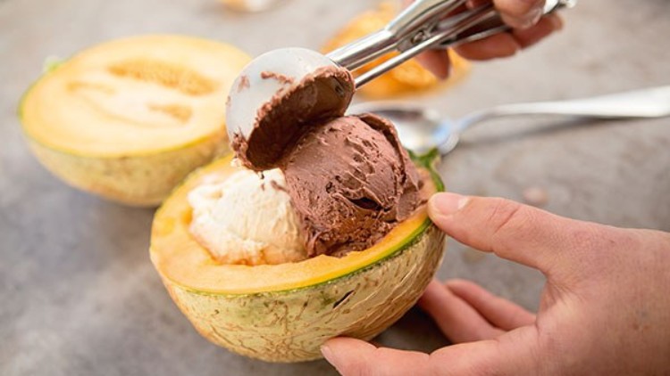 Eine halbe aufgeschnittene Melone wird mit einer Kugel Schokoladeneis und einer Kugel Vanilleeis gefüllt.