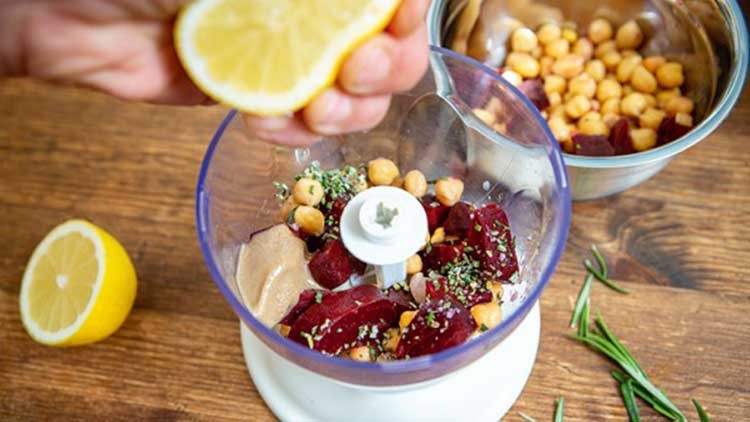 Kichererbsen, rote Bete, Gewürze und Tahini in einem Mixer, daneben Zitronensaft, Rosmarinzweige und eine Schüssel mit Kichererbsen.
