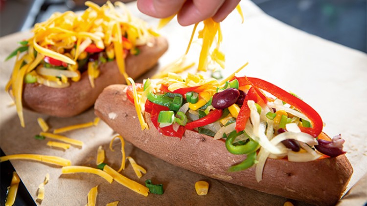 Zwei gebackene Süßkartoffeln mit Paprika, Mais, Kidneybohnen, Frühlingszwiebeln und geriebenem Käse auf braunem Backpapier.