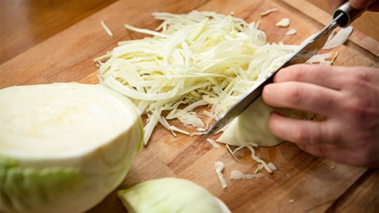 Ein Messer schneidet weißen Kohl auf einem Holzbrett, daneben liegt ein halbierter Kohlkopf.