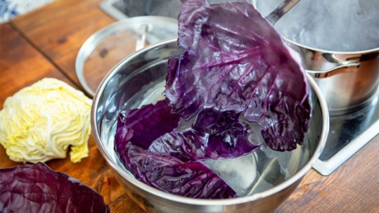 Blätter von violettem Rotkohl werden mit einem Schaumlöffel aus heißem Wasser in eine Metallschüssel gehoben, daneben liegt Wirsing.