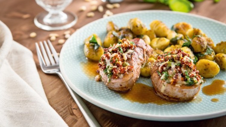 Ein Teller mit zwei Schweinefilets in Soße, belegt mit Kräutern und Tomaten, daneben goldbraune Gnocchi mit Kräutern.
