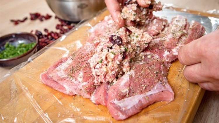 Mit Kräutern gewürztes Fleisch wird mit einer Füllung aus gehackten Nüssen, Kräutern und getrockneten Beeren per Hand befüllt.