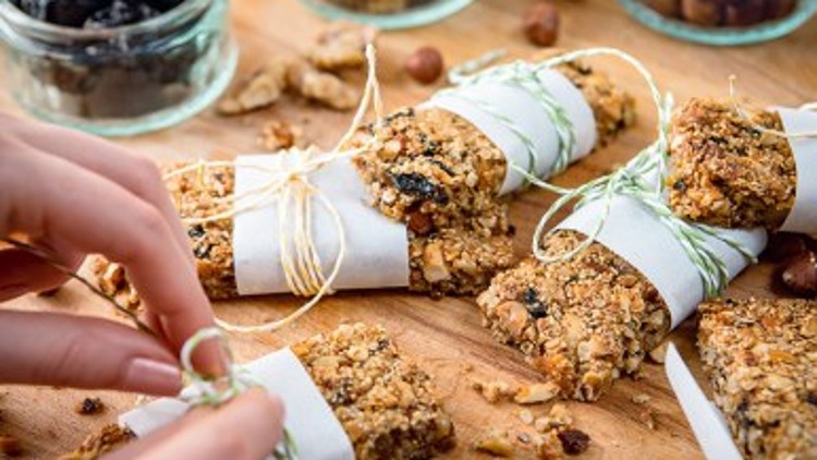Selbstgemachte Müsliriegel mit Nüssen und Trockenfrüchten werden in weißes Papier gewickelt und mit grün-weißem Faden gebunden.