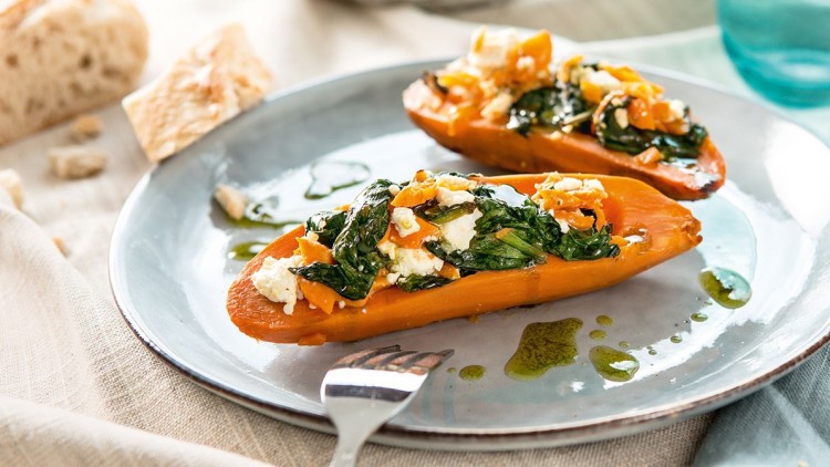 Zwei Hälften einer gebackenen Süßkartoffel mit Spinat, Feta und Karottenstreifen auf einem Teller, daneben Brot und Wasser.