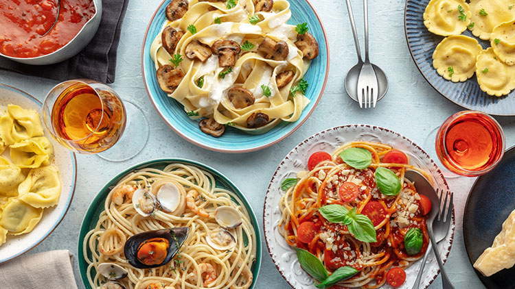Verschiedene Pastagerichte mit Saucen, garnierter Pasta und Getränken auf einem hellen Untergrund mit Besteck.