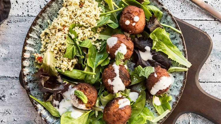Bunter Salatteller mit Falafeln, Hirse, grünen Blättern und weißem Dressing auf rustikalem Holztisch.