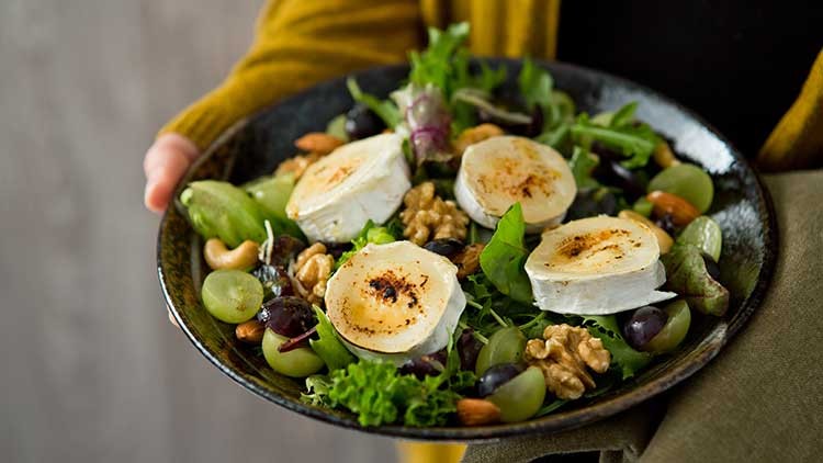 Ein Teller mit knackigem Salat, Trauben, Walnüssen, Cashewkernen und vier gebratenen Ziegenkäsescheiben.