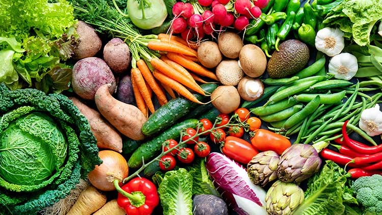 Frisches Gemüse wie Karotten, Tomaten, Paprika, Salat, Zwiebeln, Radieschen und Brokkoli liegt dicht nebeneinander.